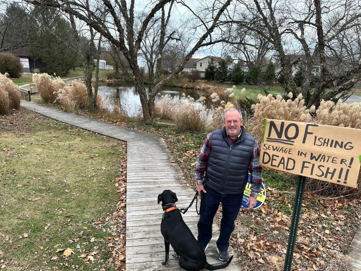 Bloomington resident Mark Combs and his dog, Luna, pose next to a sign Combs put up to warn people not to fish in a neighborhood pond after a sewage spill, though city officials said the contamination has been removed.