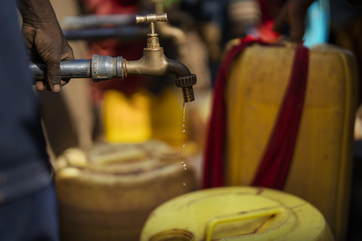 A few drops of water fall from a faucet above two dirty yellow plastic containers.