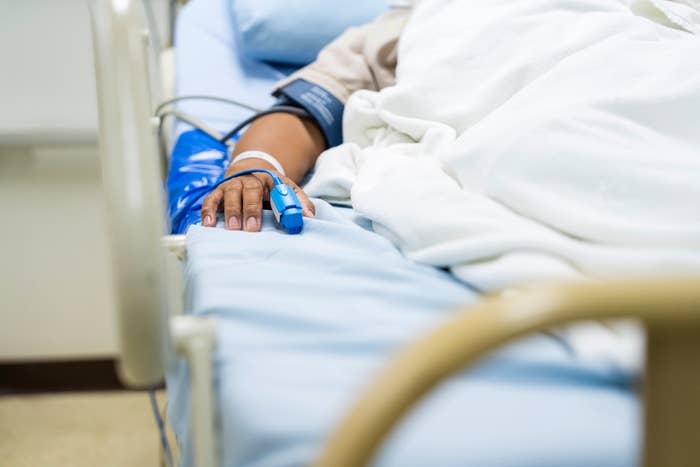 A patient lies in a hospital bed with a blood pressure cuff on their arm and a pulse oximeter clipped to their finger