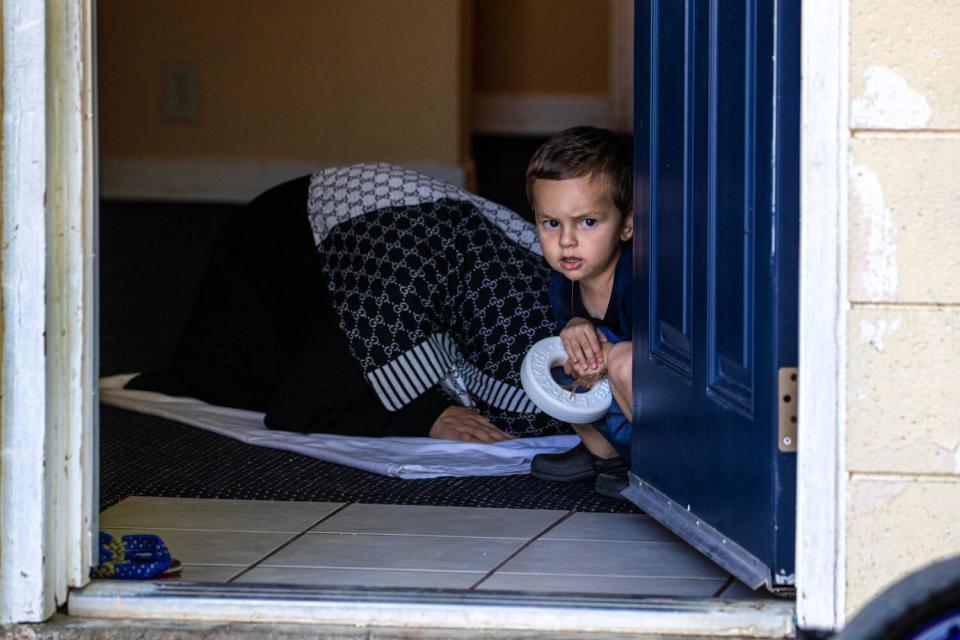 A child looks out the door as an Afghani woman offers prayers in her room