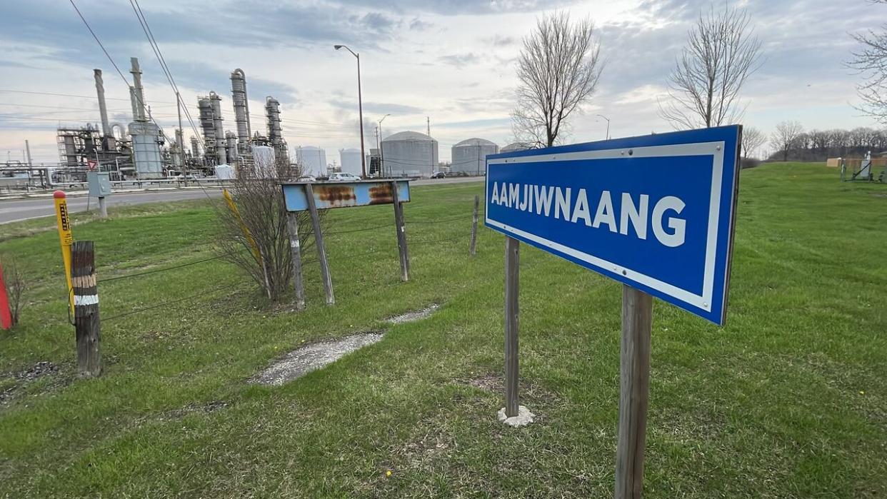 Aamjiwnaang First Nation's sign is seen in this photo taken Wednesday, with INEOS Styrolution operations in the background. The First Nation says it sent its employees homes Tuesday as they were complaining of headaches, nausea and dizziness. (Chris Ensing/CBC - image credit)