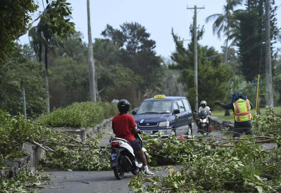 A city worker directs traffic away from trees felled by Hurricane Humberto, in the Devonshire parish of Bermuda, Thursday, Sept. 19, 2019. Humberto blew off rooftops, toppled trees and knocked out power but officials said Thursday that the Category 3 storm caused no reported deaths. (AP Photo/Akil J. Simmons)