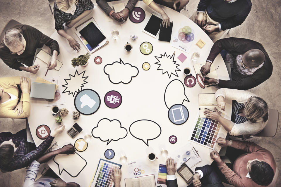 A group of people sitting at a round table full of ipads and idea bubbles.