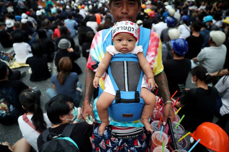 A vendor carrying a baby sells cool drinks during a protest in Bangkok