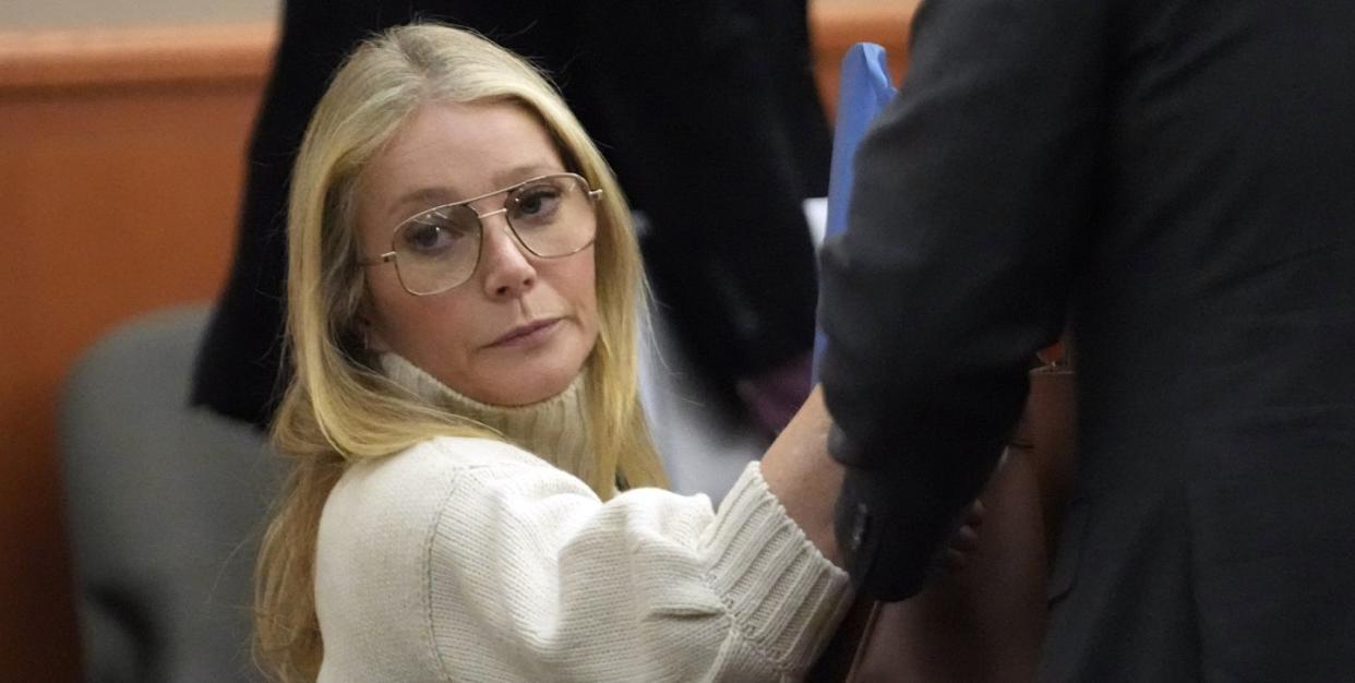 gwyneth paltrow wearing a white turtleneck sweater and glasses, sitting in a courtroom and looking ahead, unsmiling