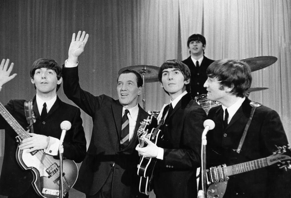 The Beatles with Ed Sullivan, posing with musical instruments before a performance