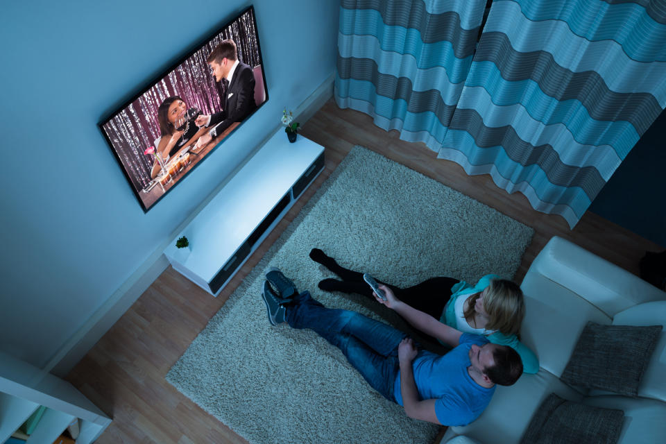 Couple watching TV in a darkened living room.