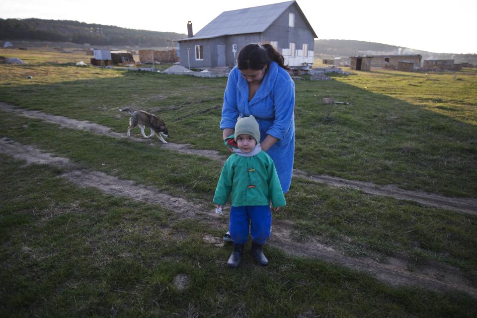 In this photo taken Thursday, March 27, 2014 Crimea's Tatar Liliya Resulova, 24, ties a scarf on her two-year-old son, Emir, outside of their recent squatter settlement, foreground, in Lozovoye-2, not far from Simferopol, Crimea. On Saturday the Crimean Tatar Qurultay, a religious congress will determine whether the Tatars will accept Russian citizenship and the political system that comes with it, or remain Ukrainian citizens on Russian soil. (AP Photo/Pavel Golovkin)