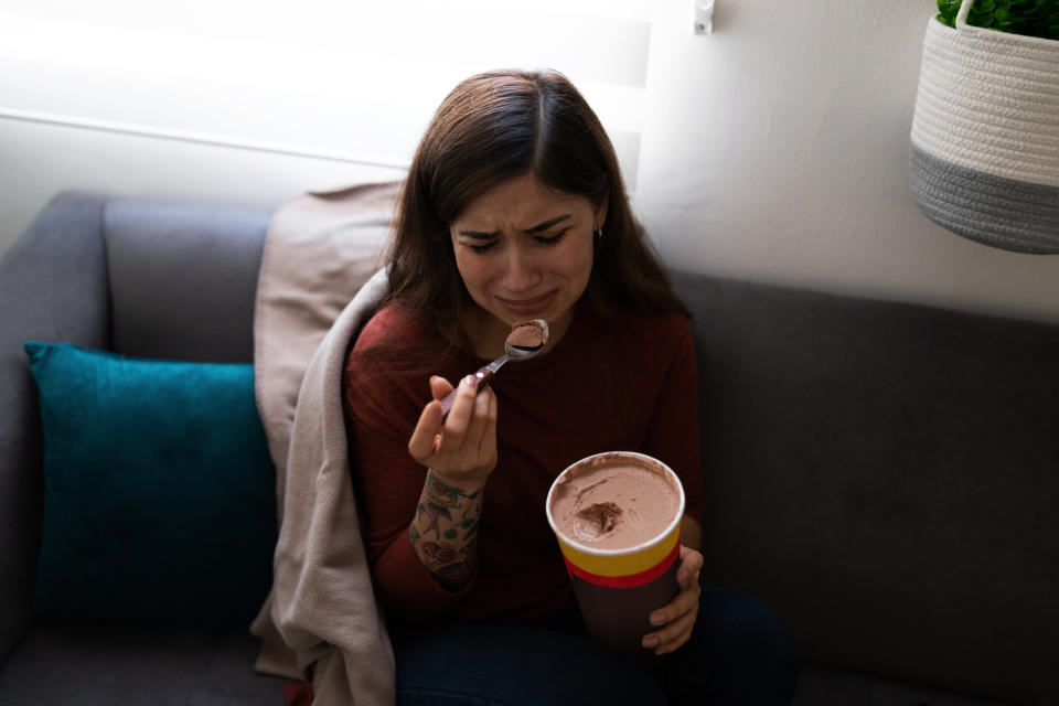 Depressed and heartbroken young woman eating ice cream while crying on the sofa. 