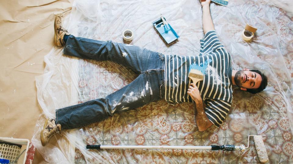 One young man is lying down on the floor after a hard days work painting his new apartment.