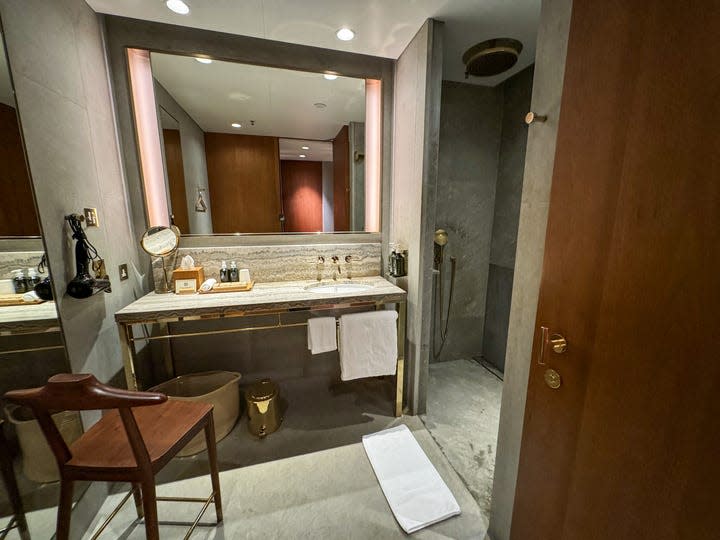 The shower suite Cathay Pacific's The Pier, a first- class lounge at Hong Kong International Airport. It has a large mirror, a sink and a dressing chair. An entrance to the large shower is on the right.