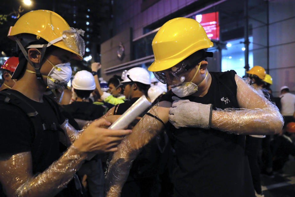 Protestors wrap their arms in plastic wrap to protect against pepper spray, as they gather near the police headquarters in Hong Kong, Friday, June 21, 2019. More than 1,000 protesters blocked Hong Kong police headquarters into the evening Friday, while others took over major streets as the tumult over the city's future showed no signs of abating. The mark on the wall is from an egg thrown by protestors. (AP Photo/Kin Cheung)