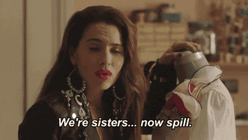 A woman looks to someone off-camera and says 'We're sisters... now spill."