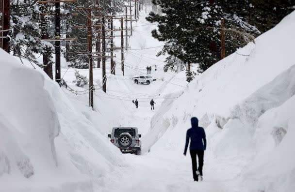 PHOTO: People make their way down a road is lined with snowbanks piled up from multiple storms, after more heavy snow fell, March 29, 2023, in Mammoth Lakes, Calif. (Mario Tama/Getty Images)