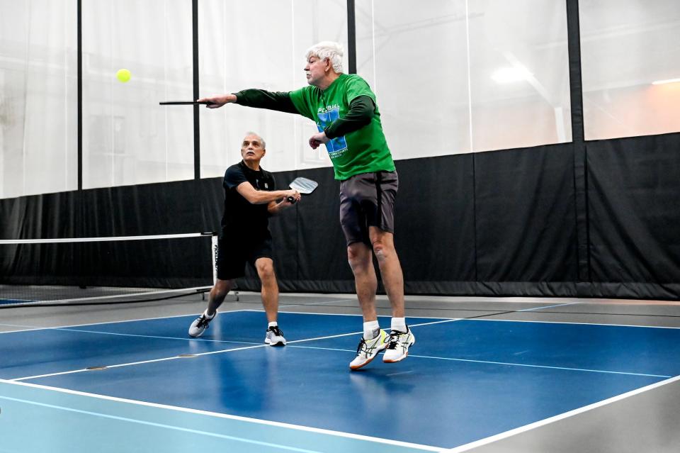 Roy Fogwell, right, returns the ball as his teammate Larry Ezzo looks on during their pickleball match on Friday, Jan. 27, 2023, at Court One Athletic Clubs in Lansing.