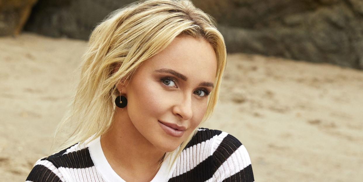 hayden panettiere sitting down on a beach towel, wearing a black and white striped top and black bikini bottoms