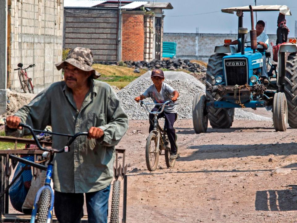 A man rides his tricycle followed by a child riding his bicycle and a tractor on April 18 in Santa Maria Jajalpa, Mexico.