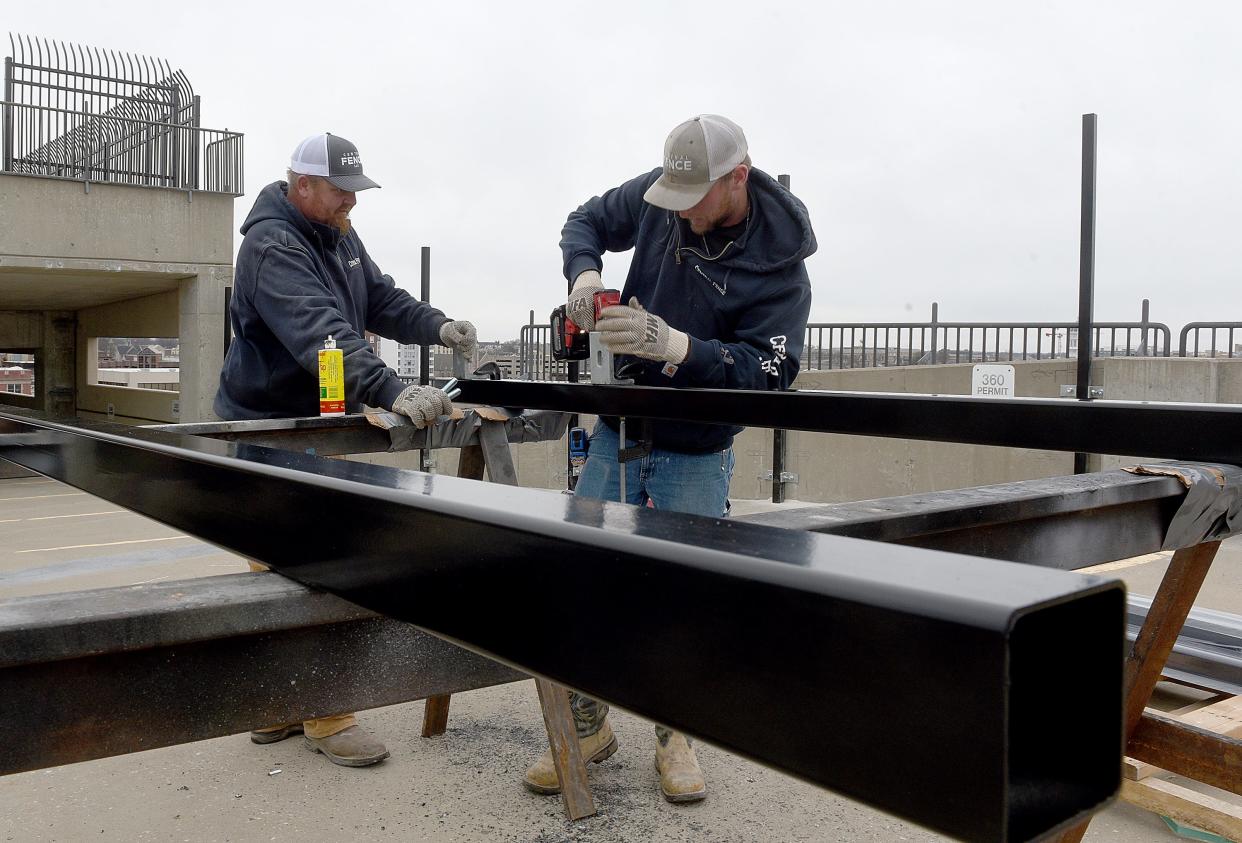 Central Fence LLC employees Tommy Pickering, left, and Kody Kleffner work on posts Friday for a ninth-floor perimeter barrier on the Fifth and Walnut parking garage. Construction of the fence is expected to be completed by the end of January. The eighth and ninth floors of the garage have been closed to the public since October. The barrier is being constructed to prevent suicide attempts after several people have jumped from various floors of the garage.