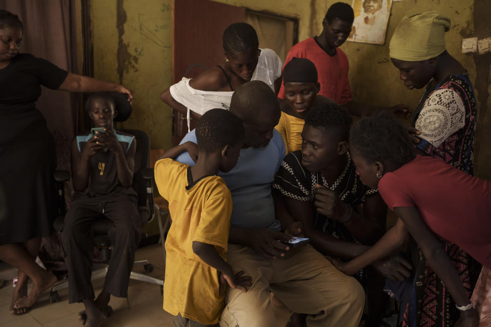 Papa Dieye, 19, center right, talks to his father Badara Dieye as they look through photographs of his rescue on a cellphone, surrounded by other relatives, in Diogo, Senegal, Monday, Aug. 28, 2023. (AP Photo/Felipe Dana)