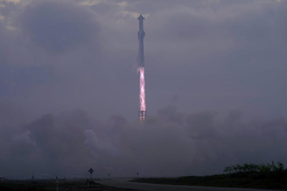 A long, cylindrical rocket with a plume of flame coming out of the tip is launched into the cloudy sky.