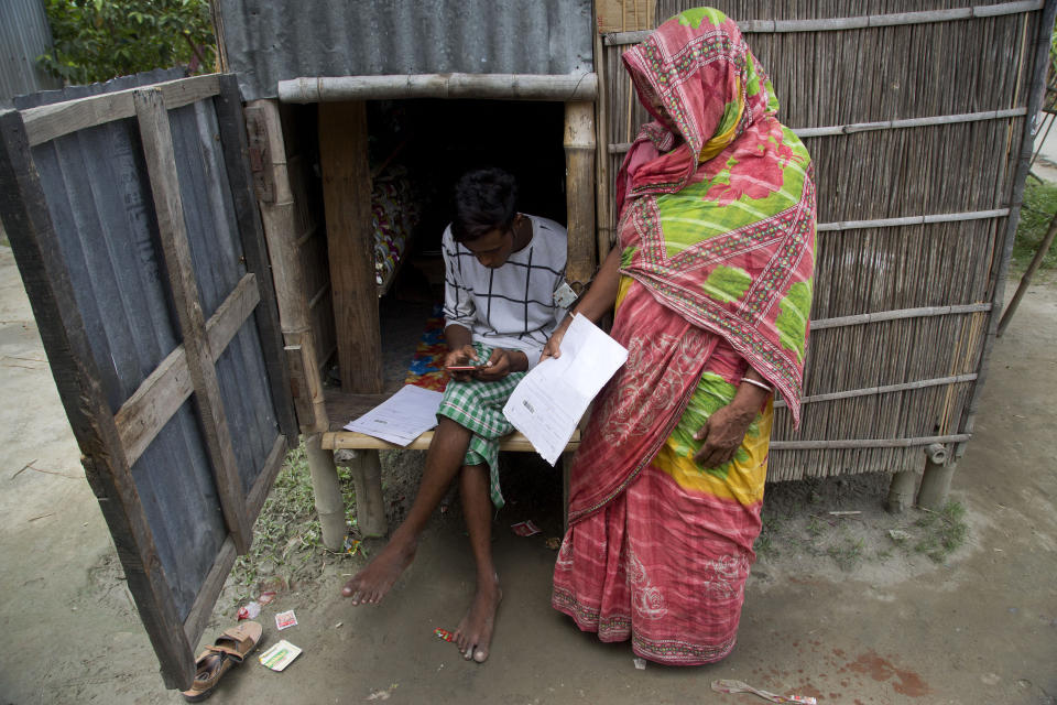 In this Aug. 31, 2019 photo, a man checks names in the final list of National Register of Citizens on his mobile phone as a woman stands waiting to check her name in Buraburi village, Morigaon district, Assam, India. About 1.9 million people were left out of the National Register of Citizens _ a mammoth exercise to weed out illegal mainly Bangladeshi immigrants from Assam’s more than 32 million people. (AP Photo/Anupam Nath)