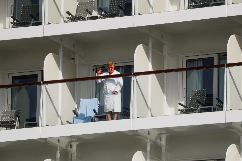 This image shows a person in a robe waving from a balcony of a cruise ship.