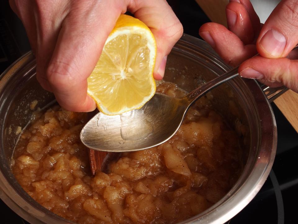 person squeezing lemon over a spoon on top of a bowl of food