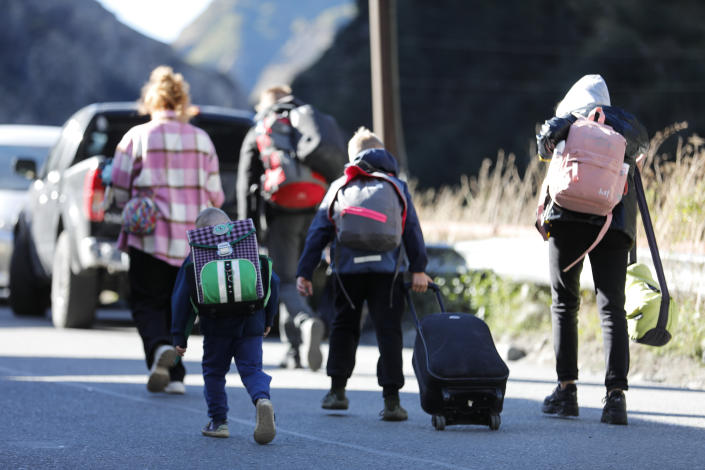 Russian adults and children carry backpacks and wheel luggage as they walk on a road toward Georgia.