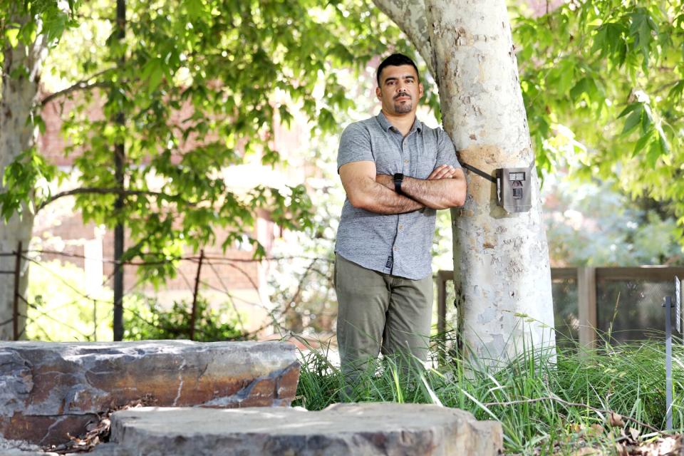 A man leans against a tree with a camera tied to it