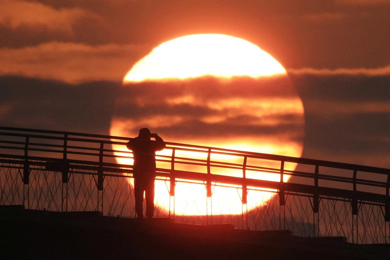 A man on a bridge takes photograph of the first sunrise of the year at a park in Seoul, South Korea, 1 January 2024 (Reuters)