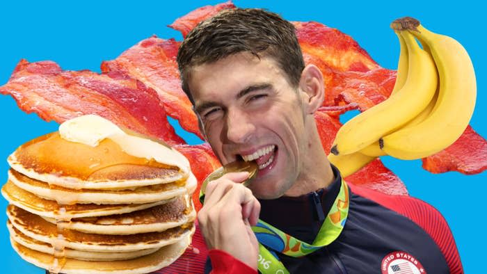 Michael Phelps, wearing a medal, biting it with bananas, pancakes, and bacon in the background