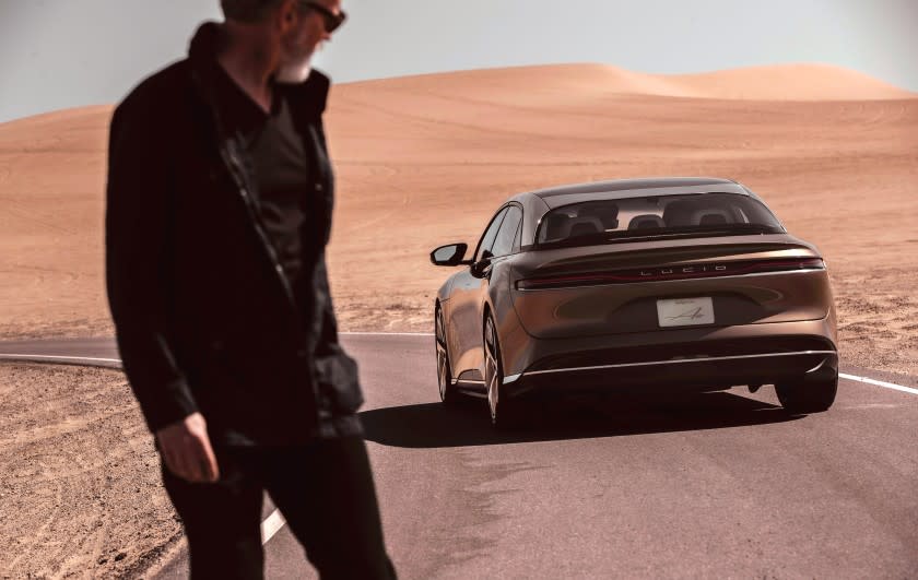 An unidentified man in a flat desert scene looks at a Lucid Air electric car in a 2020 promotional photograph.