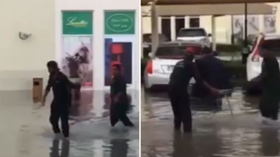 Two workers wade through the knee-deep water to help the man get to his car. Photo: YouTube