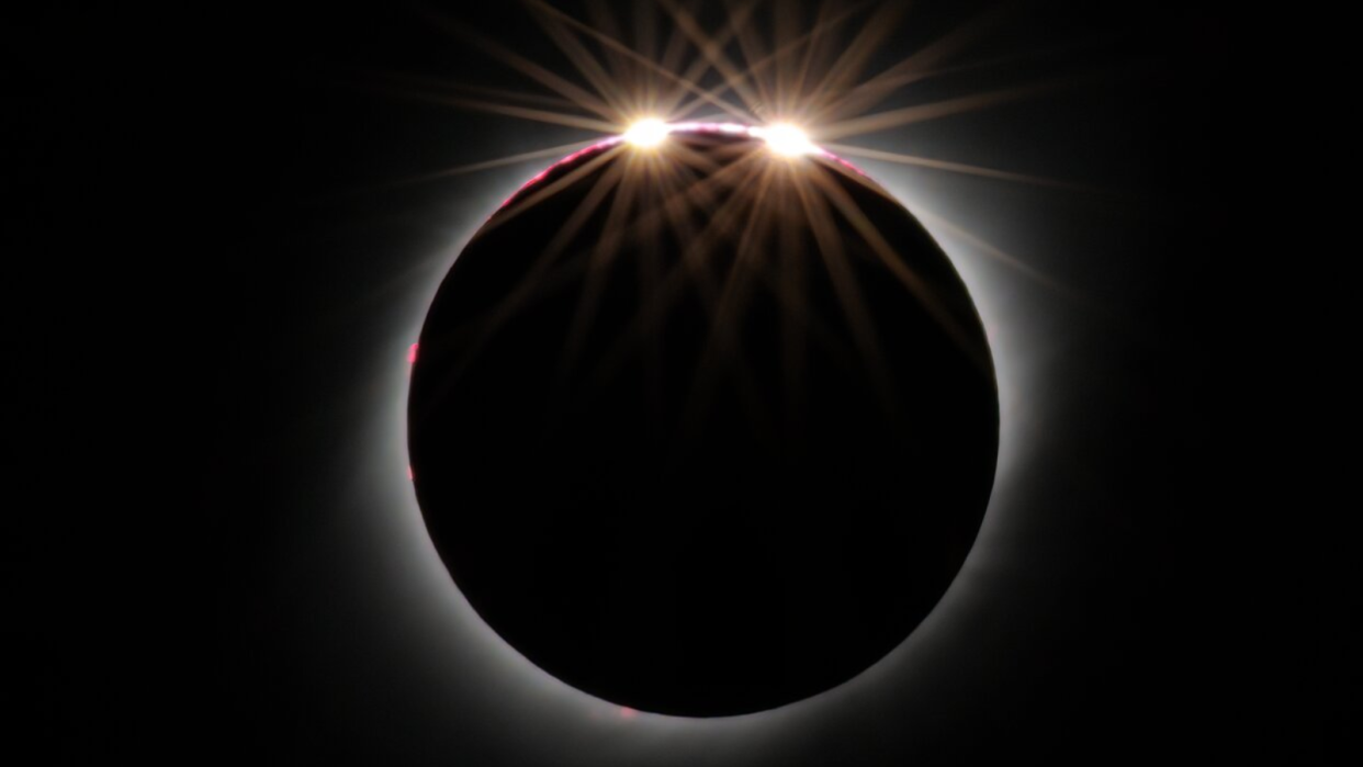  A solar eclipse, showing the darkened solar disk with two bright points of light shining on the edge. 