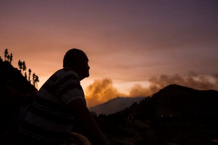 A resident who was evacuated from his home looks at the forest fire seen in the village of Valleseco