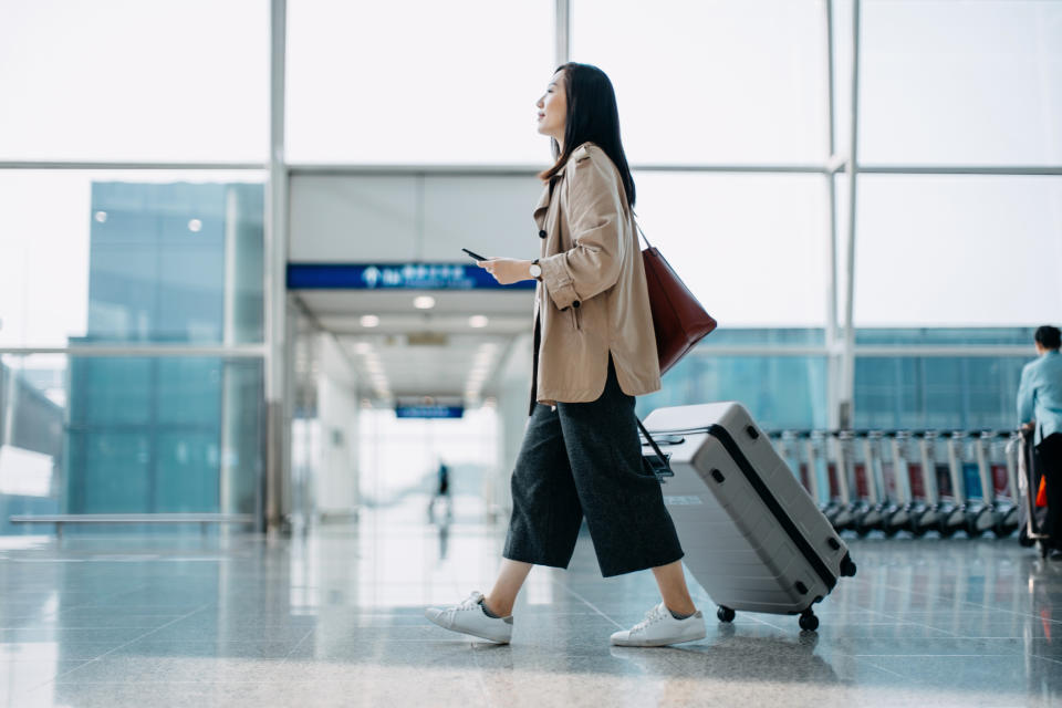 Person walking in airport with luggage, holding passport and boarding pass