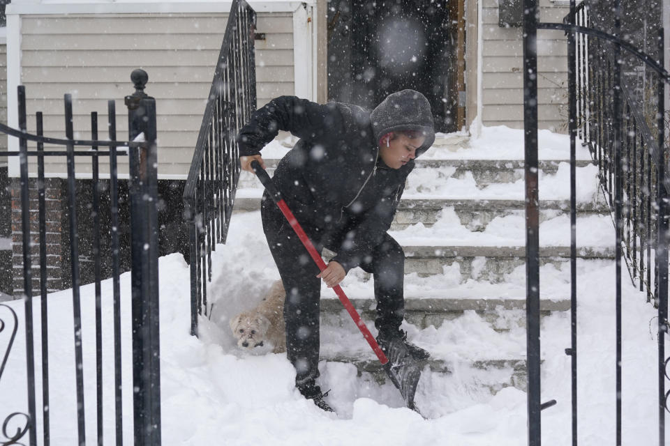 Skye DeJesus shovels her stairs while her dog Gordo pokes around in the snow in Jersey City, N.J., Monday, Feb. 1, 2021. A sprawling, lumbering winter storm is walloping the Eastern U.S., shutting down coronavirus vaccination sites, closing schools and halting transit. (AP Photo/Seth Wenig)