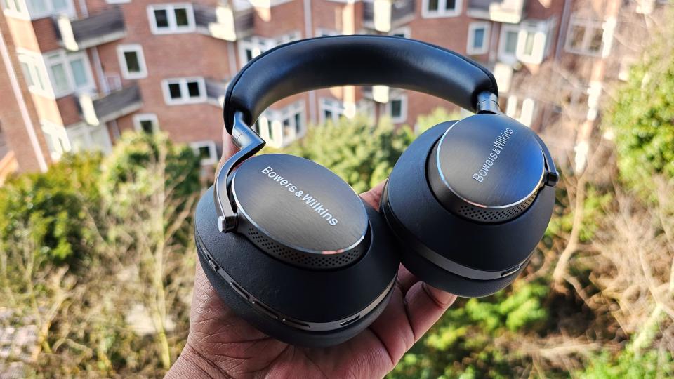 Someone holding the Bowers & Wilkins PX8 over-ear headphones in black over green foliage.