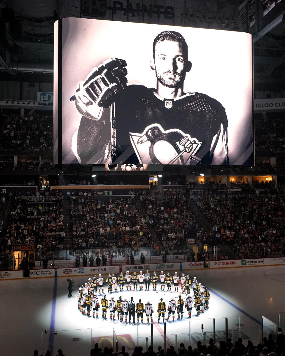 The Pittsburgh Penguins and Anaheim Ducks gather at center ice, before an NHL hockey game in Pittsburgh, Monday, Oct. 30, 2023, to honor former Penguin player Adam Johnson, shown on the scoreboard, who died in a "freak accident" while playing in an English hockey league game. (AP Photo/Gene J. Puskar)