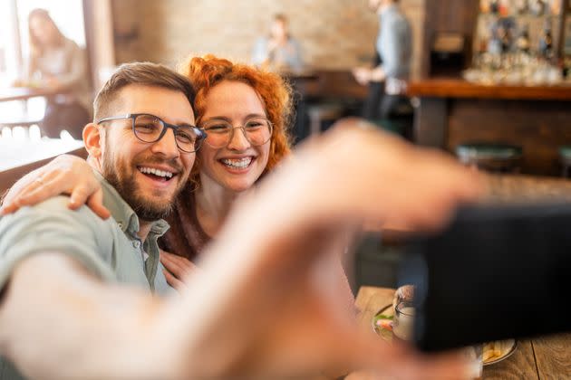 Young couple taking a selfie while eating at a restaurant (Photo: Zorica Nastasic via Getty Images)