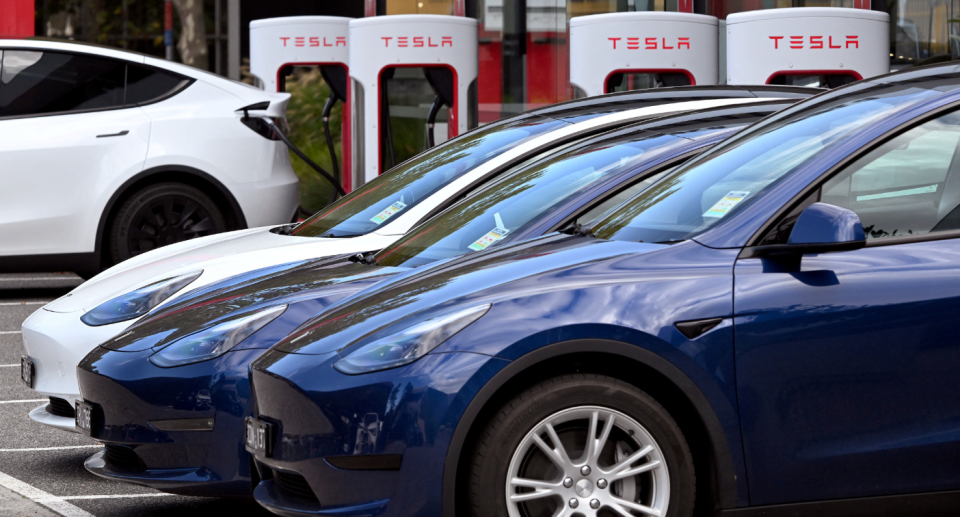 Image of Tesla cars lined up near Tesla charging stations. 