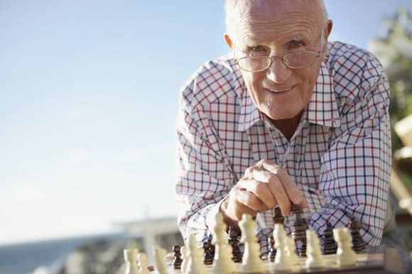 An elderly man playing chess near the beach.