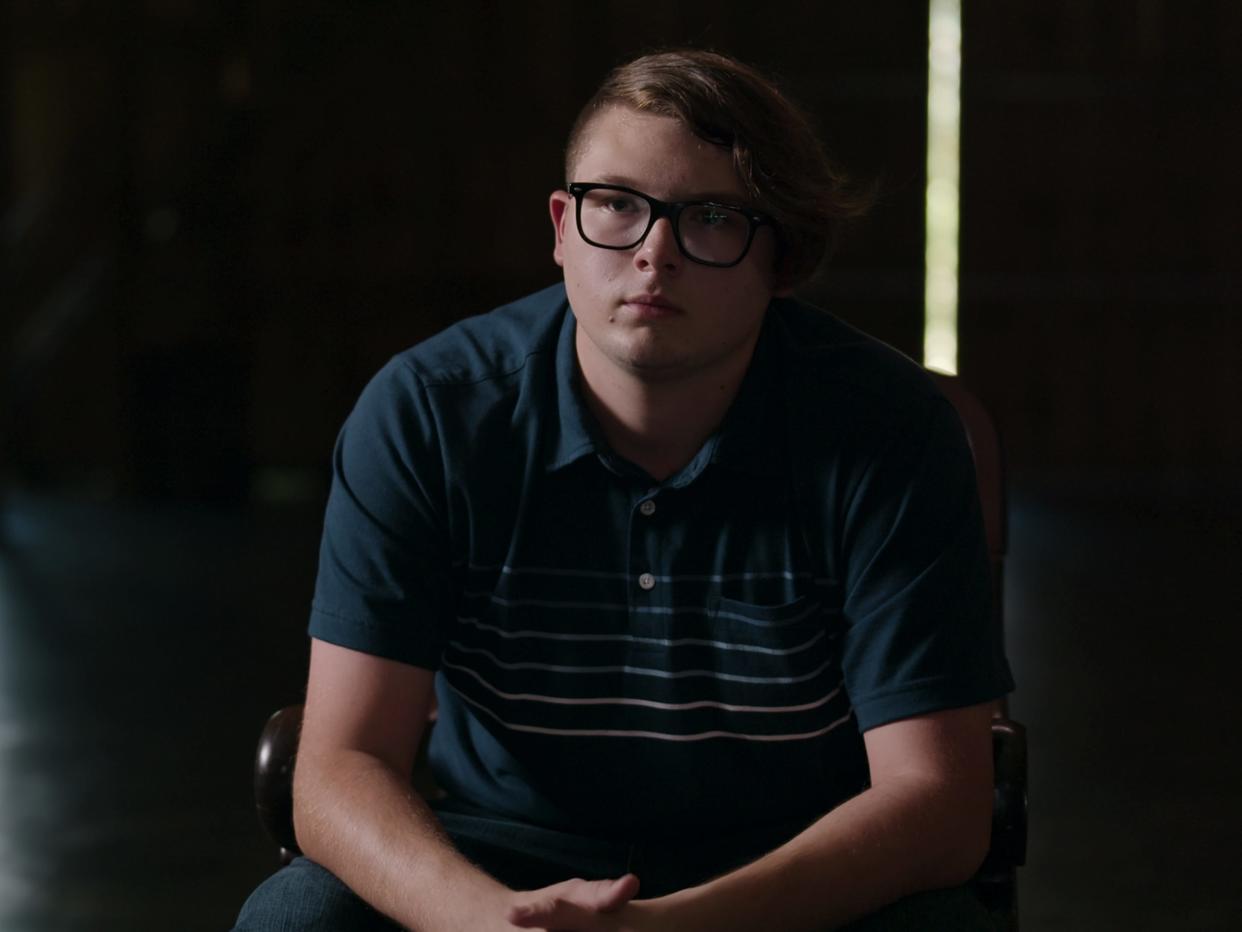 Anthony Templet, the subject of the Netflix documentary, "I Killed My Father," speaks during an interview in the film, sitting in a chair in a sparse room. He is wearing a dark blue shirt.