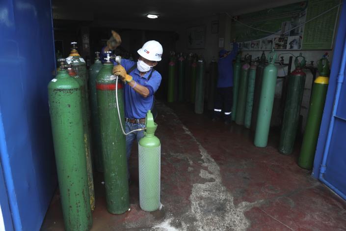 A worker wearing a mask to prevent the spread of the new coronavirus refills an empty oxygen cylinder in Callao, Peru, Wednesday 3, 2020. Long neglected hospitals in Peru and other parts of Latin America are reporting shortages of Oxygen as they confront the COVID-19 pandemic. (AP Photo/Martin Mejia)