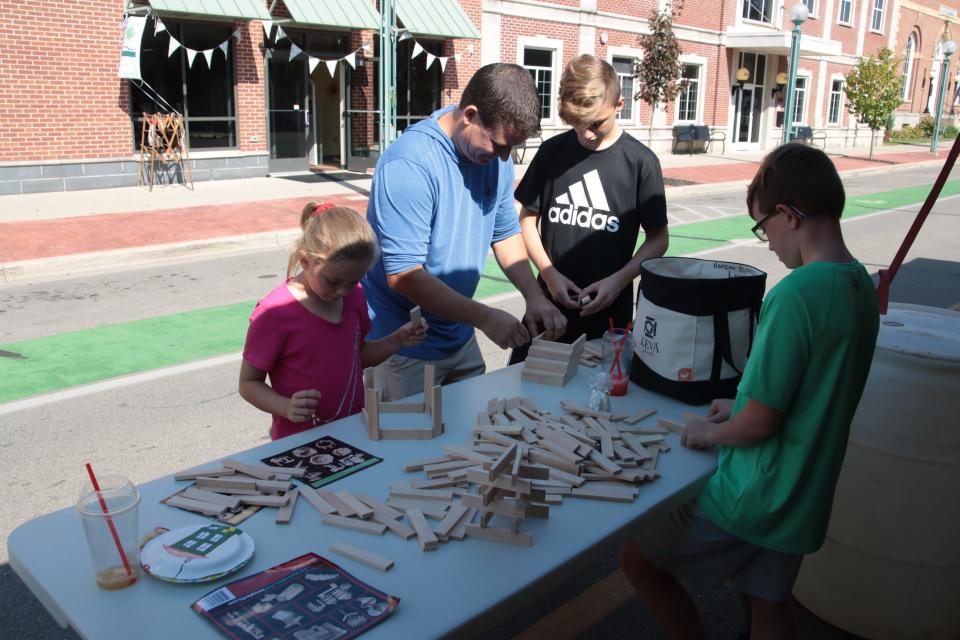From left, Harmony Powell, 8, Eric Powell, Anias Powell, 13, and Myles Powell, 10, all of Adrian, work with Keva Planks Sept. 18, 2021, at the Adrian District Library's tent at Artalicious in downtown Adrian.
