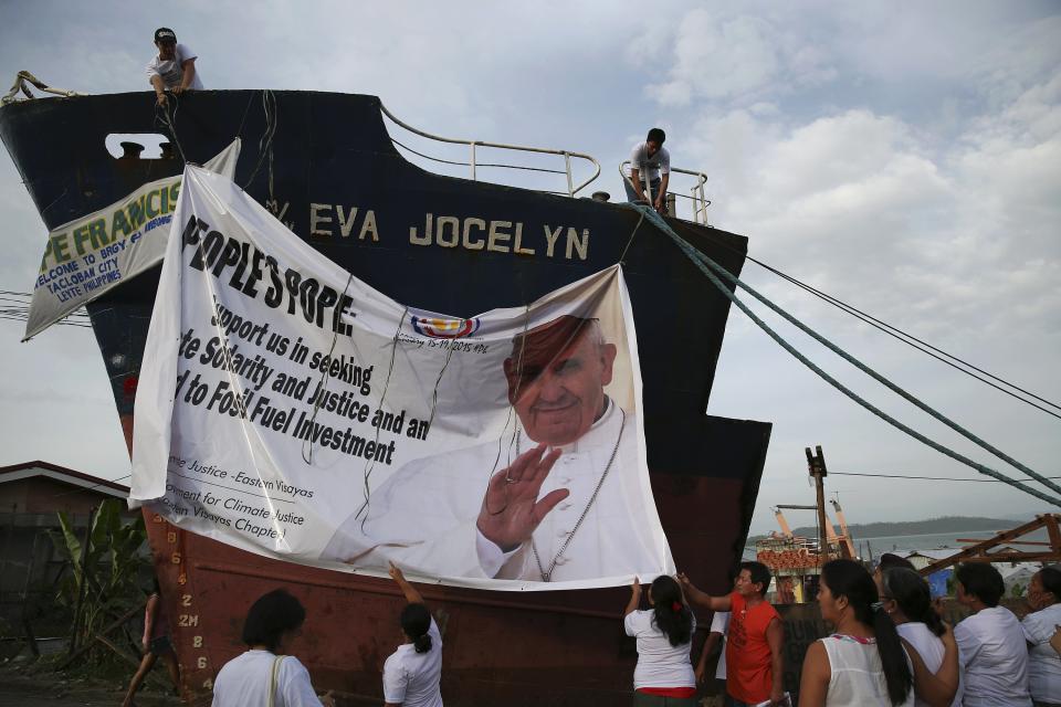 Members of an environmentalist group hang a banner, asking Pope Francis for support, onto the remains of a ship brought inland by Typhoon Haiyan in Tacloban