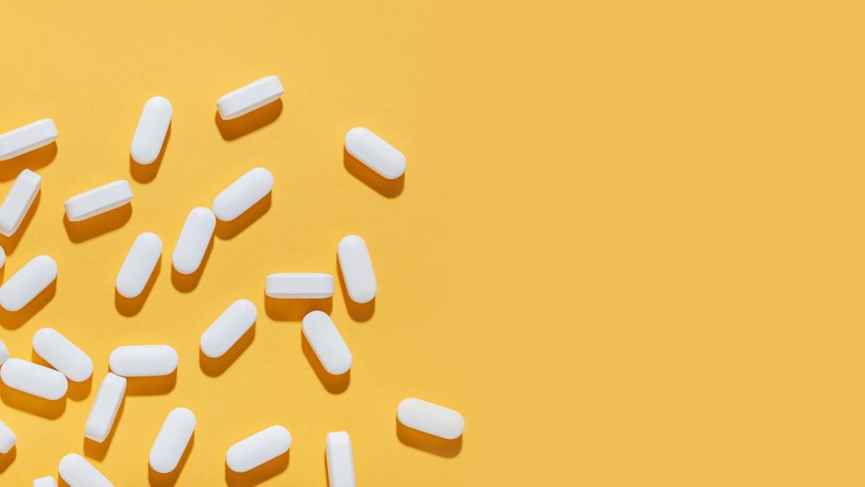 white pills are poured from a jar on a yellow background food supplement, multivitamins, medications