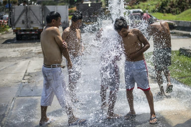 Men take a shower with water from a municipal cistern in Lima on March 18, 2017 after weeks of heavy rain came sweeping toward the Peruvian coast and filled many riverbeds in coastal areas that went from empty to overflowing in no time