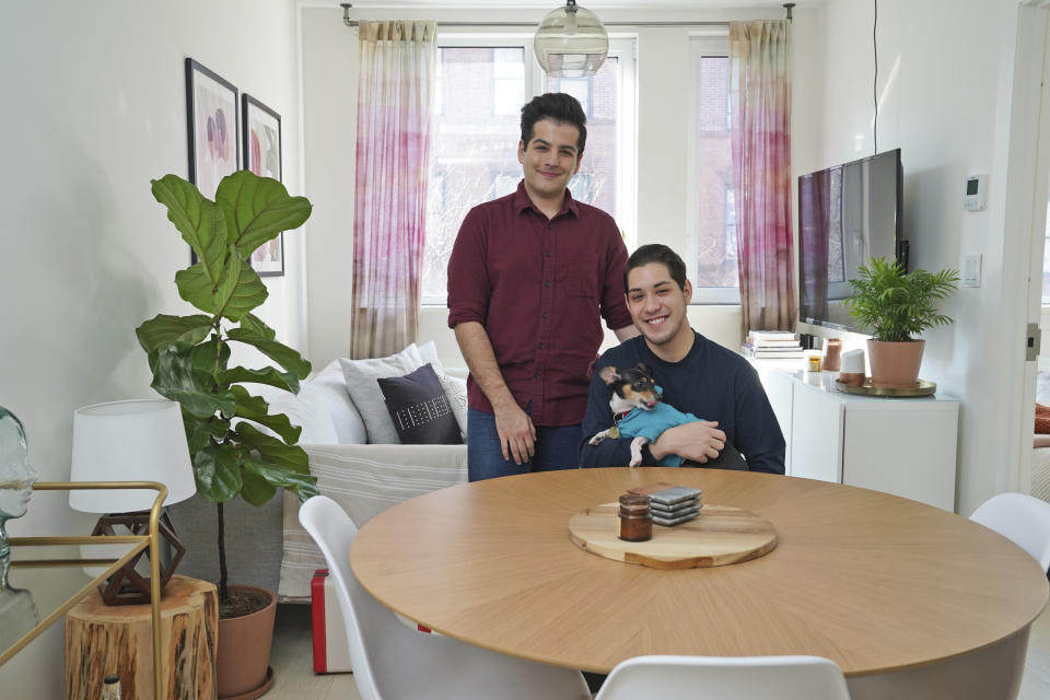 In this Monday, Nov. 25, 2019 photo, Zachariah Mohammed, left, Pete Mancilla, and their dog Remy pose for a picture in their apartment in New York. Most of the furniture in their apartment, including the couch, the table and chairs, the side table and the bar cart, are rented. Furniture-rental startups and other companies are aiming to rent furniture to millennials who don't want to commit to big purchases or move heavy furniture and are willing to pay for the convenience. (AP Photo/Seth Wenig)