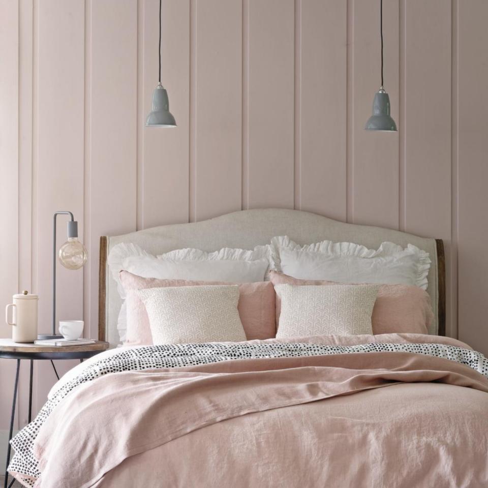 A small pink bedroom with the double bed in focus (curved headboard in white)